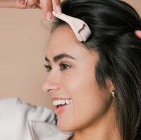 A woman smiling while using a HAIRLOVE Derma Roller on her scalp.