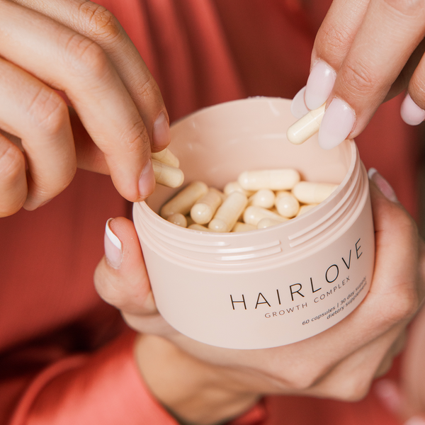 Hands holding open HAIRLOVE jar labeled GROWTH COMPLEX containing beige supplement capsules.