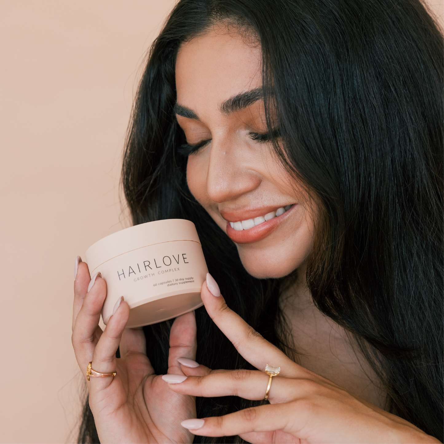 A woman smiling while holding a jar of HAIRLOVE Growth Complex, which is labeled with the product name.