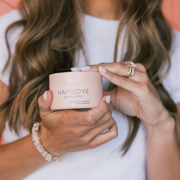 Hands holding a pink jar labeled HAIRLOVE growth complex 60 capsules 30 day supply dietary supplement