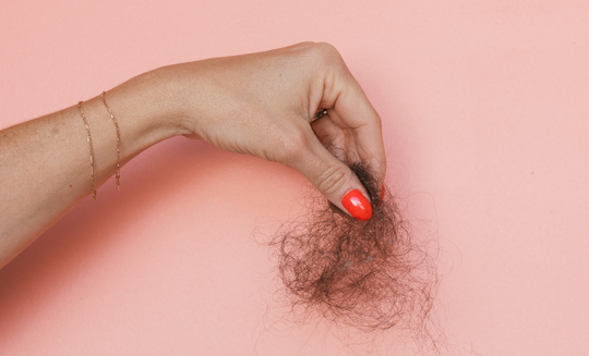 Hand with bright red nail polish holding a clump of shed hair against a pink background