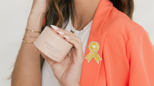 Woman holding a HAIRLOVE jar wearing coral blazer with yellow endometriosis awareness ribbon