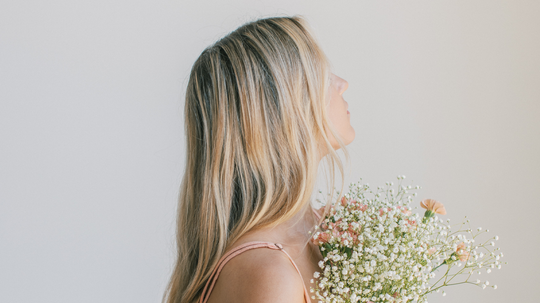 Woman in profile holding a bouquet of baby’s breath, showing long blonde hair against a pale background