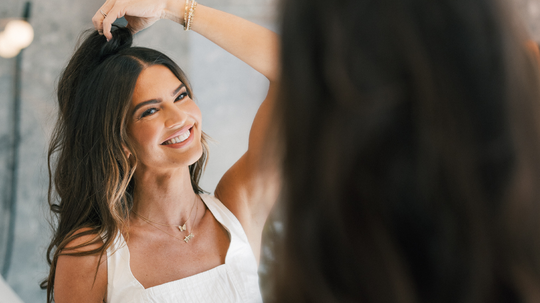Smiling woman lifting her hair while looking at herself in a mirror in a bright room