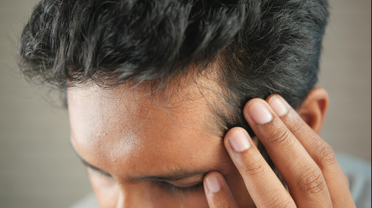 Close-up of a man touching his receding hairline, showing thinning hair at the temples