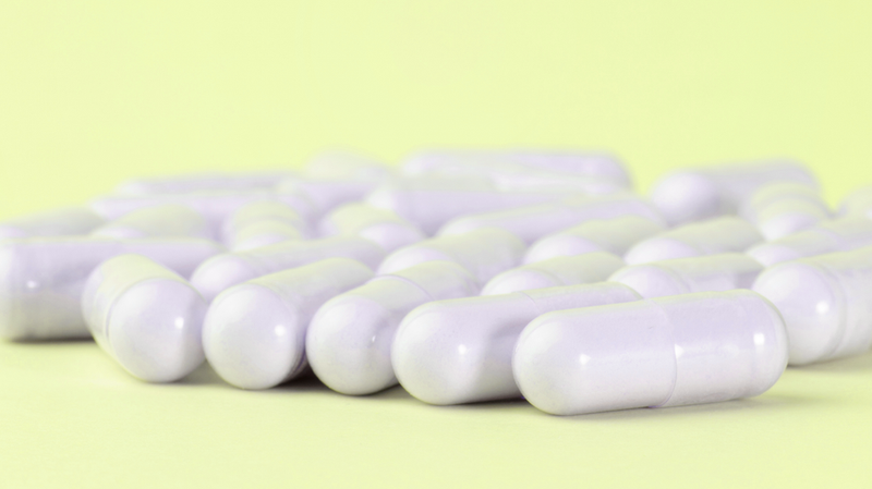 Close-up of pale lavender supplement capsules scattered on a soft yellow background