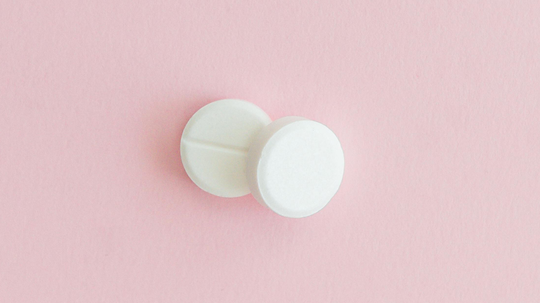 Two white round tablets on a pink background representing prescription medication for an article about Wellbutrin and hair loss