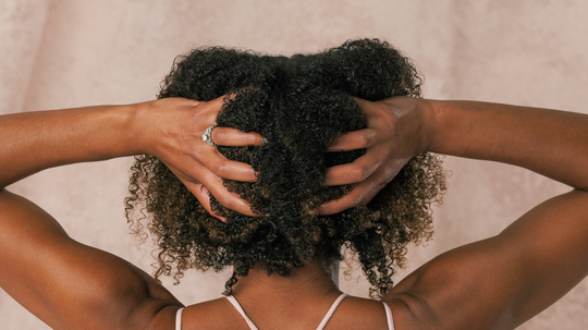 Rear view of a person gathering natural curly hair with both hands against a soft beige background