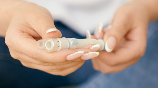 Close-up of hands holding a medication injection pen before self-injection with a soft blurred background