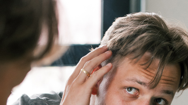 Man inspecting thinning hair in a mirror, focusing on a receding hairline