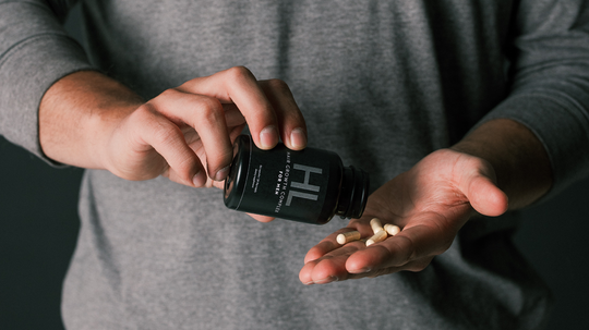 Person pouring hair growth supplement capsules from a black HL bottle into their palm against a dark background