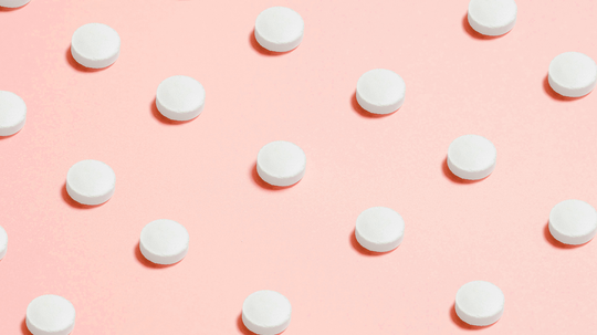 White round tablets evenly spaced on a pink background