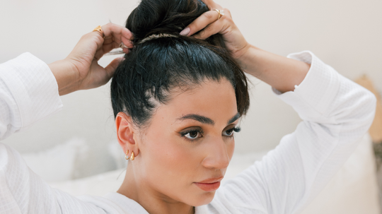 Woman gathering her hair into a high bun in a bright bedroom setting