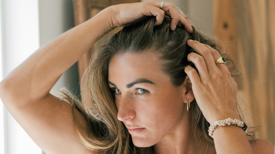 Woman pulling back her long brown hair to reveal her scalp in a sunlit indoor setting