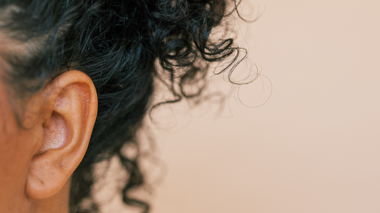 Close-up of a person’s curly dark hair and ear against a pale pink background