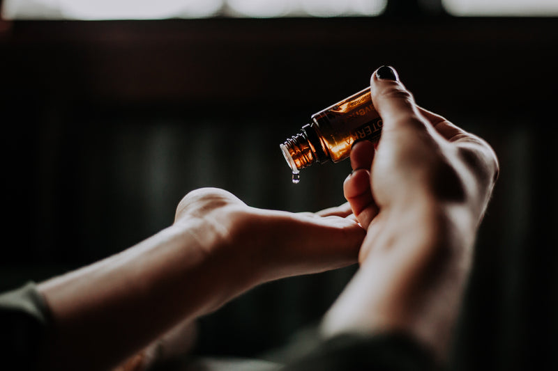 A person pouring argan oil from a bottle into their palm.