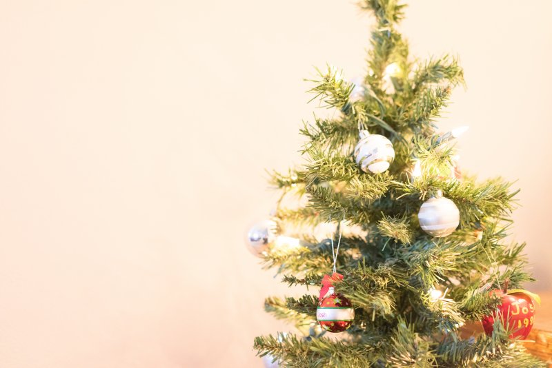 Small Christmas tree decorated with white and red ornaments and warm white string lights against a beige wall