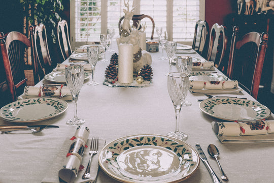 Holiday dining table set with festive plates, crystal glasses, napkins, and a candle-and-pinecone centerpiece