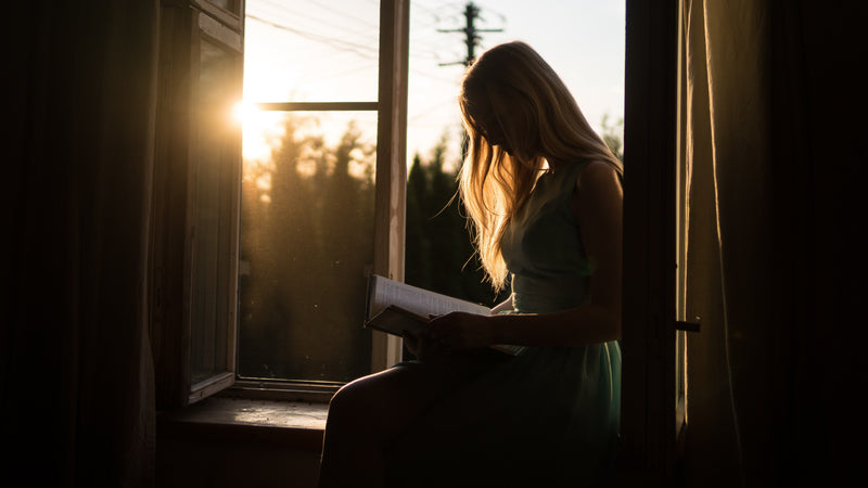 Woman reading on a windowsill, silhouetted by warm sunset light