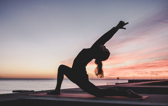 Woman performing crescent moon yoga pose on a mat by the sea at sunset