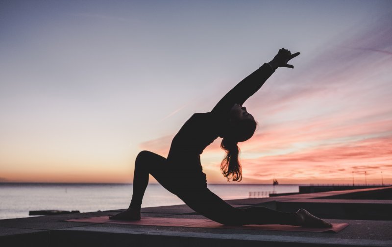 Woman performing crescent moon yoga pose on a mat by the sea at sunset