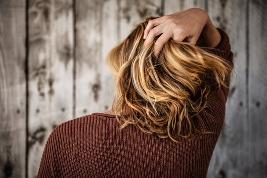 Person with shoulder-length blonde hair scrunching hair with hand against a rustic wooden background