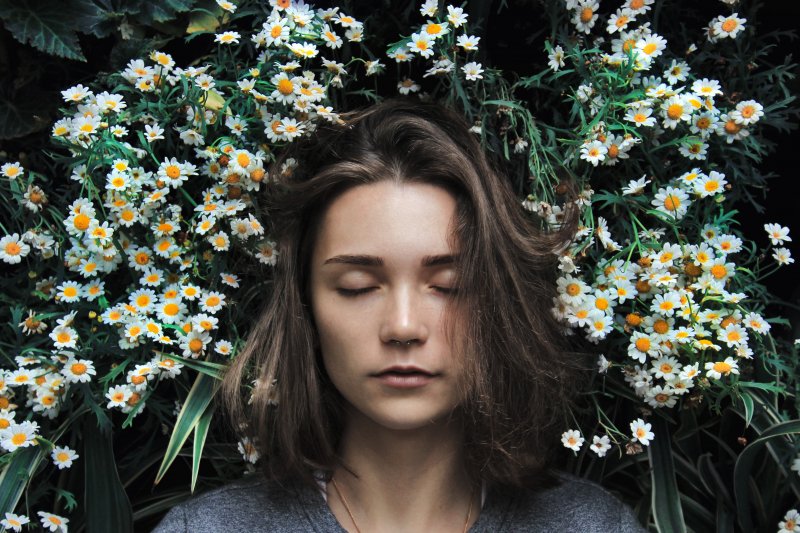 A woman with closed eyes surrounded by chamomile flowers, conveying tranquility.