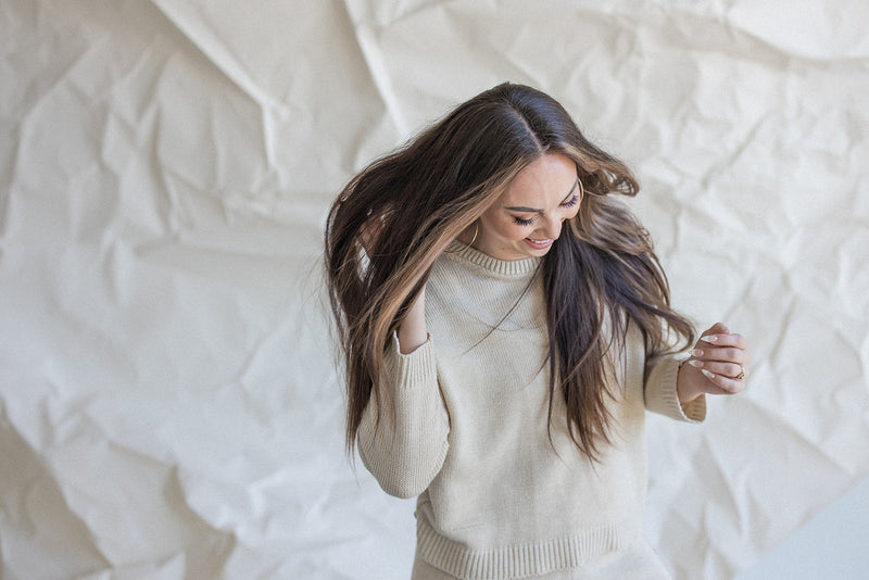 A woman with long hair smiling and playing with her hair against a textured background.