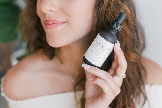 Close-up of HAIRLOVE Nourish + Repair Serum dropper bottle held by a smiling woman, label visible and blurred background