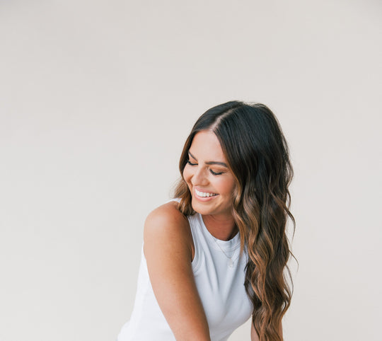 Woman smiling and looking down with long wavy brown hair against a plain light background