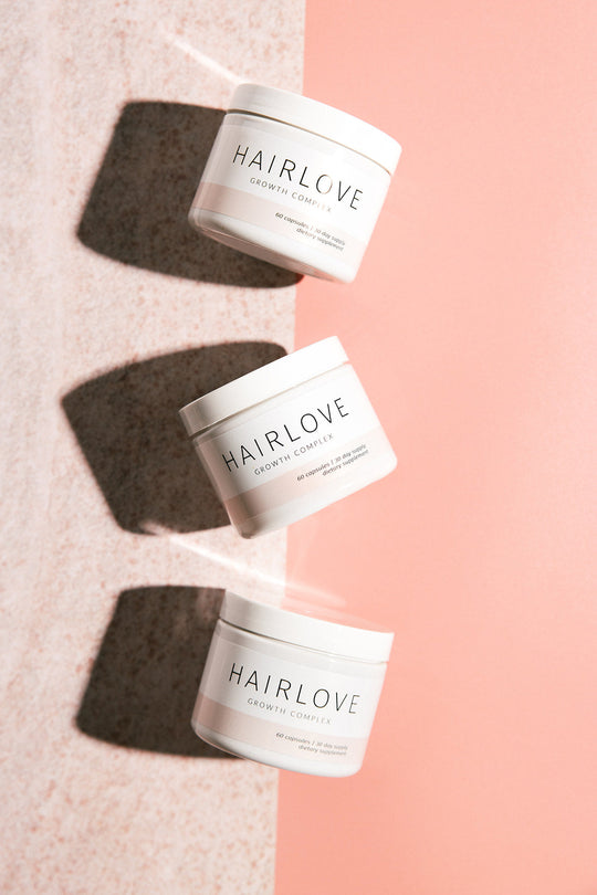 Angled overhead view of three HAIRLOVE Growth Complex jars showing label text and shadows on a split pink and beige background