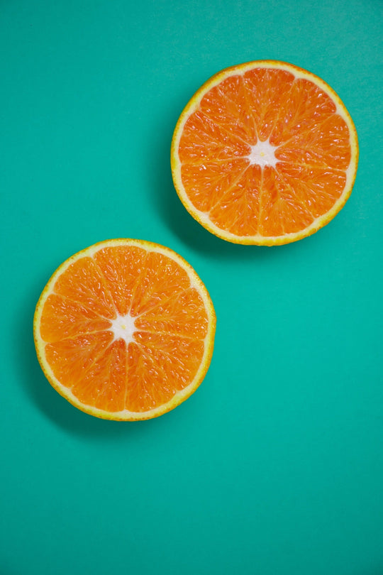 Two halved oranges on teal background representing vitamin C benefits for hair and skin