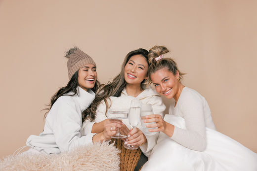 Three women smiling and toasting with glasses of water in a warm neutral studio setting promoting healthy hair routines