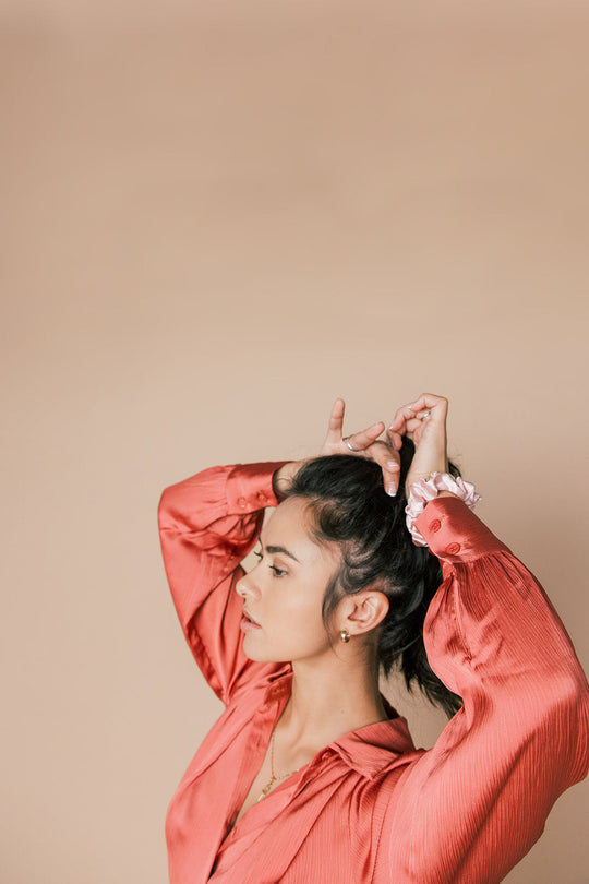 Woman in a coral blouse adjusting her hair against a beige background