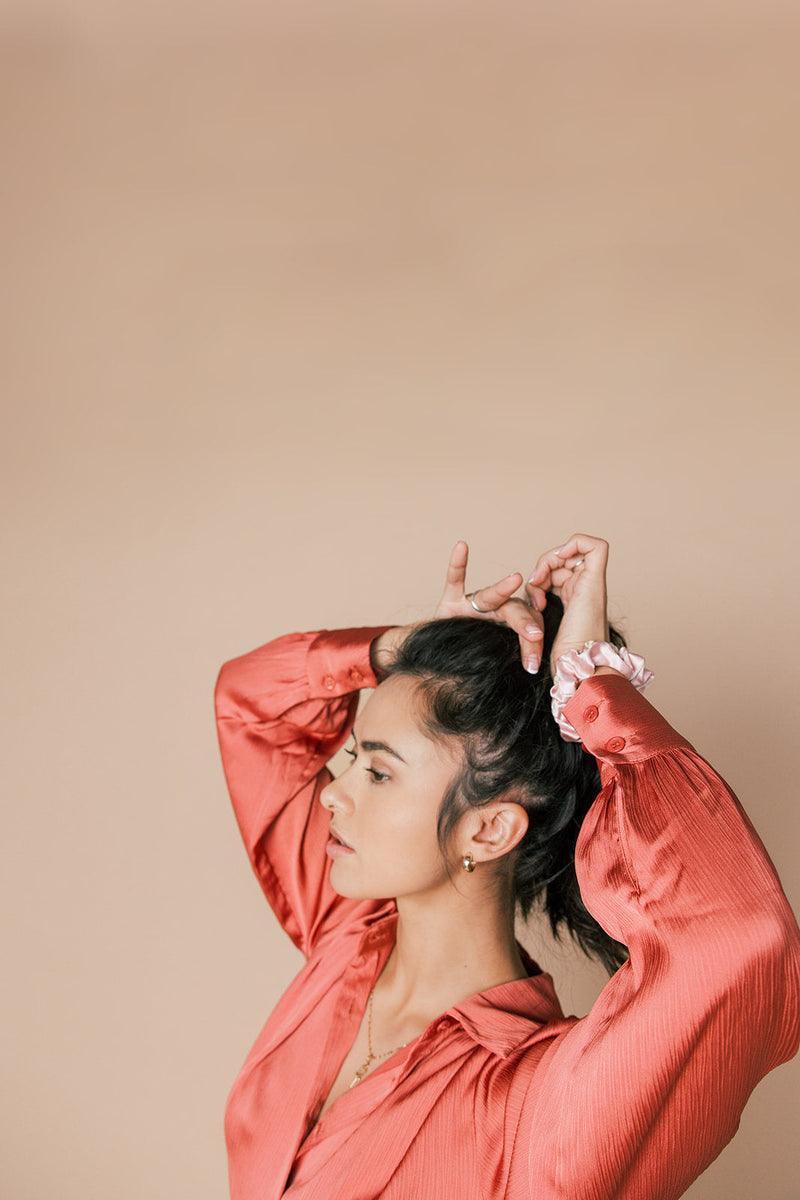 Woman in a coral blouse adjusting her hair against a beige background