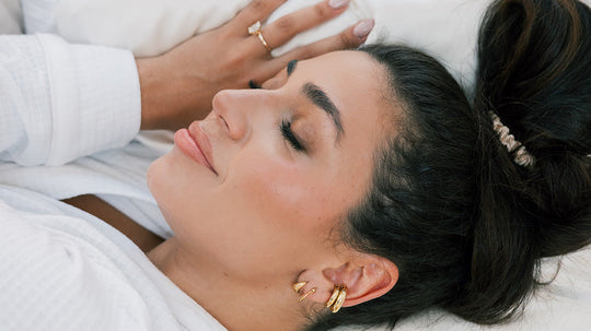 Woman sleeping on her side with hair in a loose bun, wearing a white robe and gold hoop earrings on a white pillow