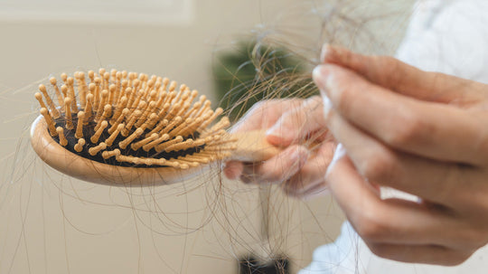 Close-up of a wooden hairbrush with many strands of hair caught in its bristles and a hand holding loose hair strands, illustrating female hair loss.