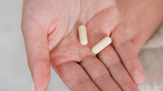 Close-up of two beige supplement capsules resting in a hand showing pill size and texture against a neutral background