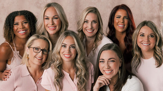 Eight women smiling, showing diverse hair types and styles against a soft pink backdrop