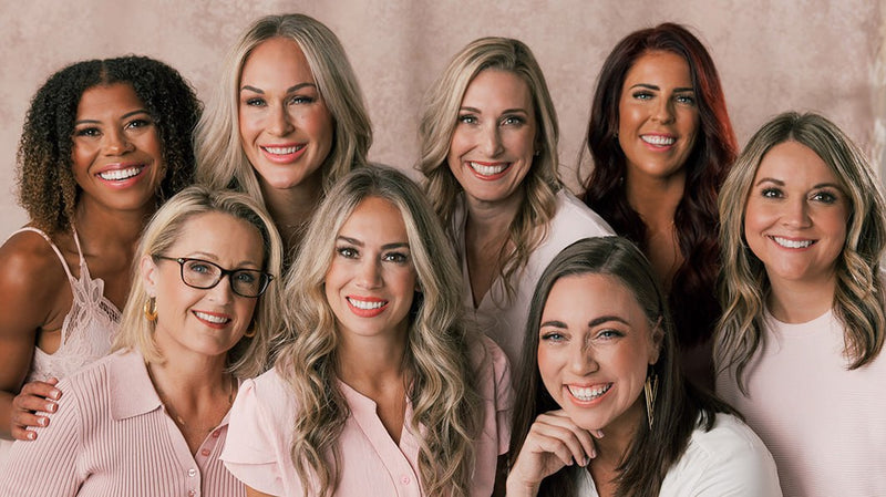 Eight women smiling, showing diverse hair types and styles against a soft pink backdrop
