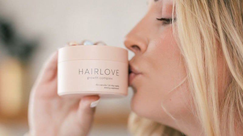 Blonde woman kissing a jar of HAIRLOVE Growth Complex supplement in a soft-focus indoor setting