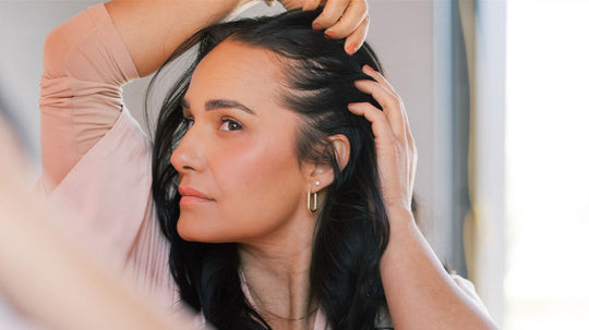 Woman touching her hairline and scalp, looking contemplative in a softly lit indoor setting