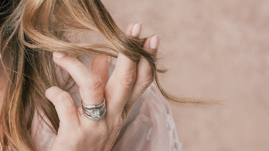 Close-up of a hand with silver rings holding a strand of dry, split blonde hair.
