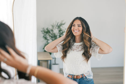 Smiling young woman adjusting her hair while looking into a mirror in a bright, minimal room