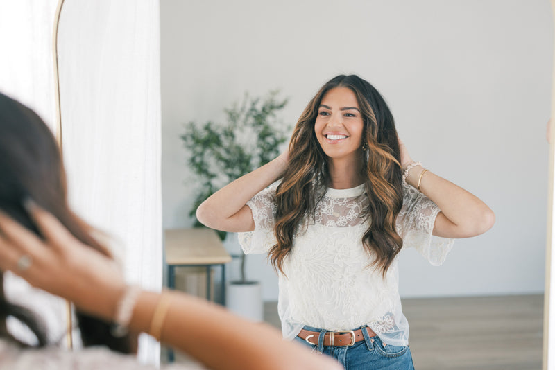Smiling young woman adjusting her hair while looking into a mirror in a bright, minimal room