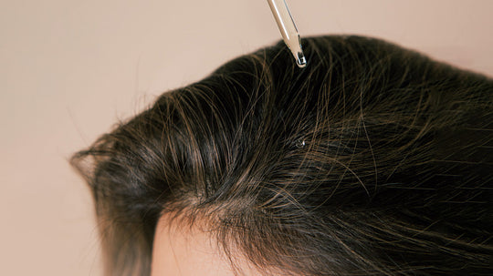 Close-up of a scalp and hair part with a glass dropper releasing a droplet