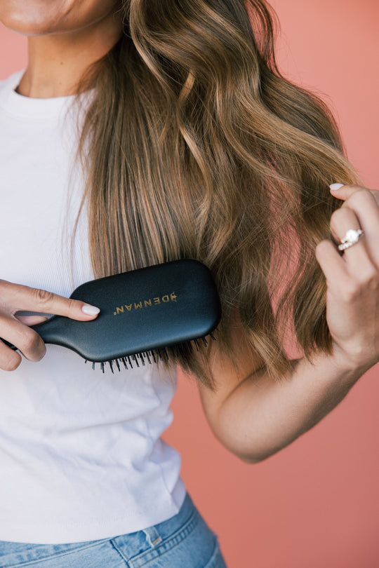 Woman brushing long highlighted hair with a black brush labeled DENMAN