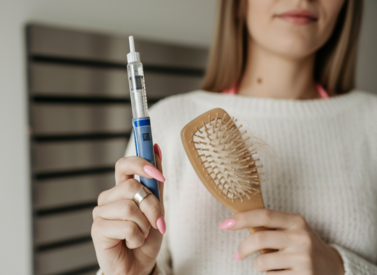 Woman holding an injection pen and a hairbrush with strands of shed hair, illustrating medication-related hair loss