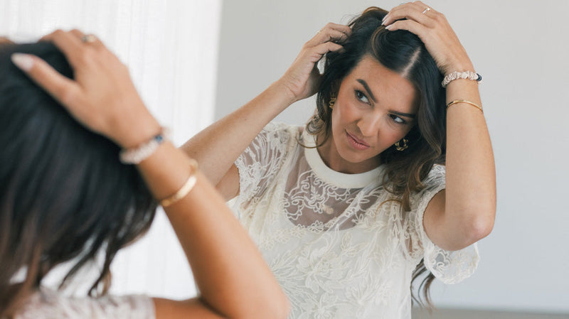 Woman parting her hair and inspecting her scalp in a mirror with a concerned expression