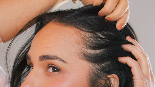 Close-up of a person parting dark hair to reveal the scalp and hairline